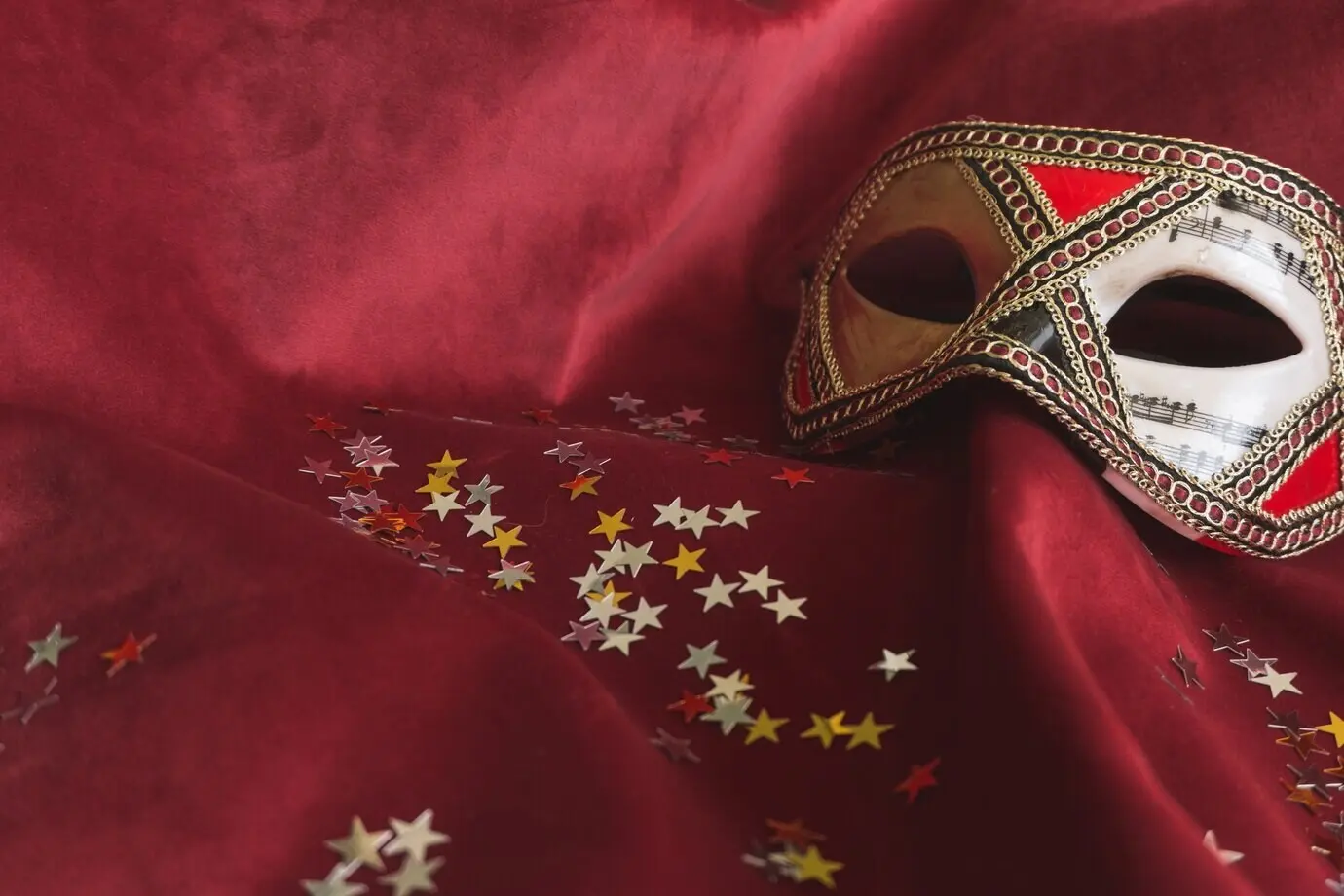 Venezianische Maske auf rotem Stoff mit Sternkonfetti.